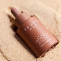 The H7 face tanning serum bottle resting in sand