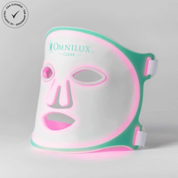 Omnilux Clear flexible LED light therapy mask illuminated in pink, shown at an angle