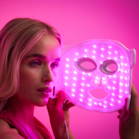 Woman relaxing while wearing the Omnilux Clear mask during a pink LED light therapy session