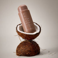 The gradual tan moisturizer bottle resting on a halved coconut