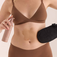 A person wearing the application mitt on one hand and holding a bottle of Brown Bee self-tanner in the other