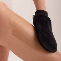 A black application mitt sweeping self-tanning mousse along a lower leg
